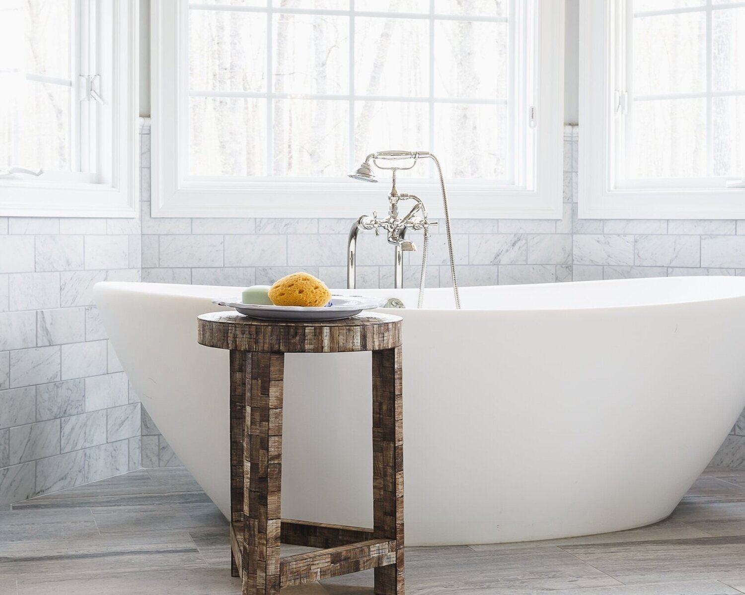 Stylish modern bathroom featuring a freestanding tub and wooden table with bath accessories.